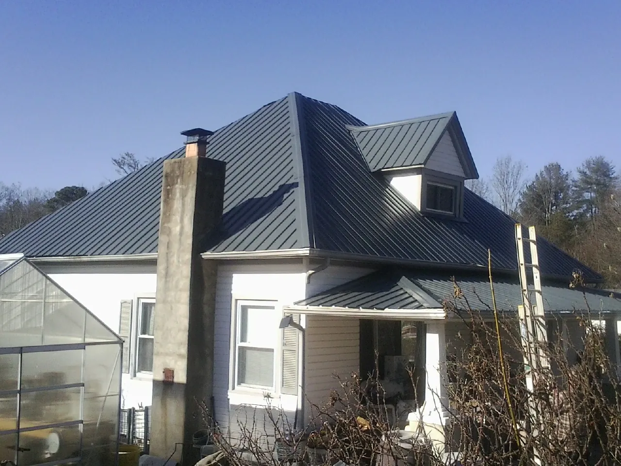 Dark blue standing seam metal roof on a white farmhouse with dormer — Slate & Tile Roof Repair by Roofing Brothers in Nelsonville