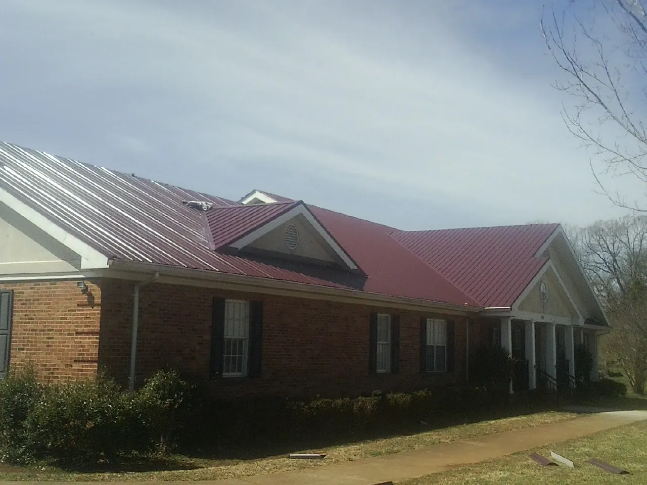 Red metal roof with gabled entries on a long brick building, from a Hail Damage Roof Repair job in Nelsonville