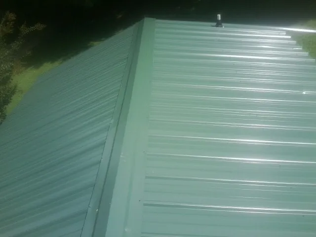 New green metal panels meeting at the ridge of a roof — Flat Roof Repair work by our crew in Nelsonville