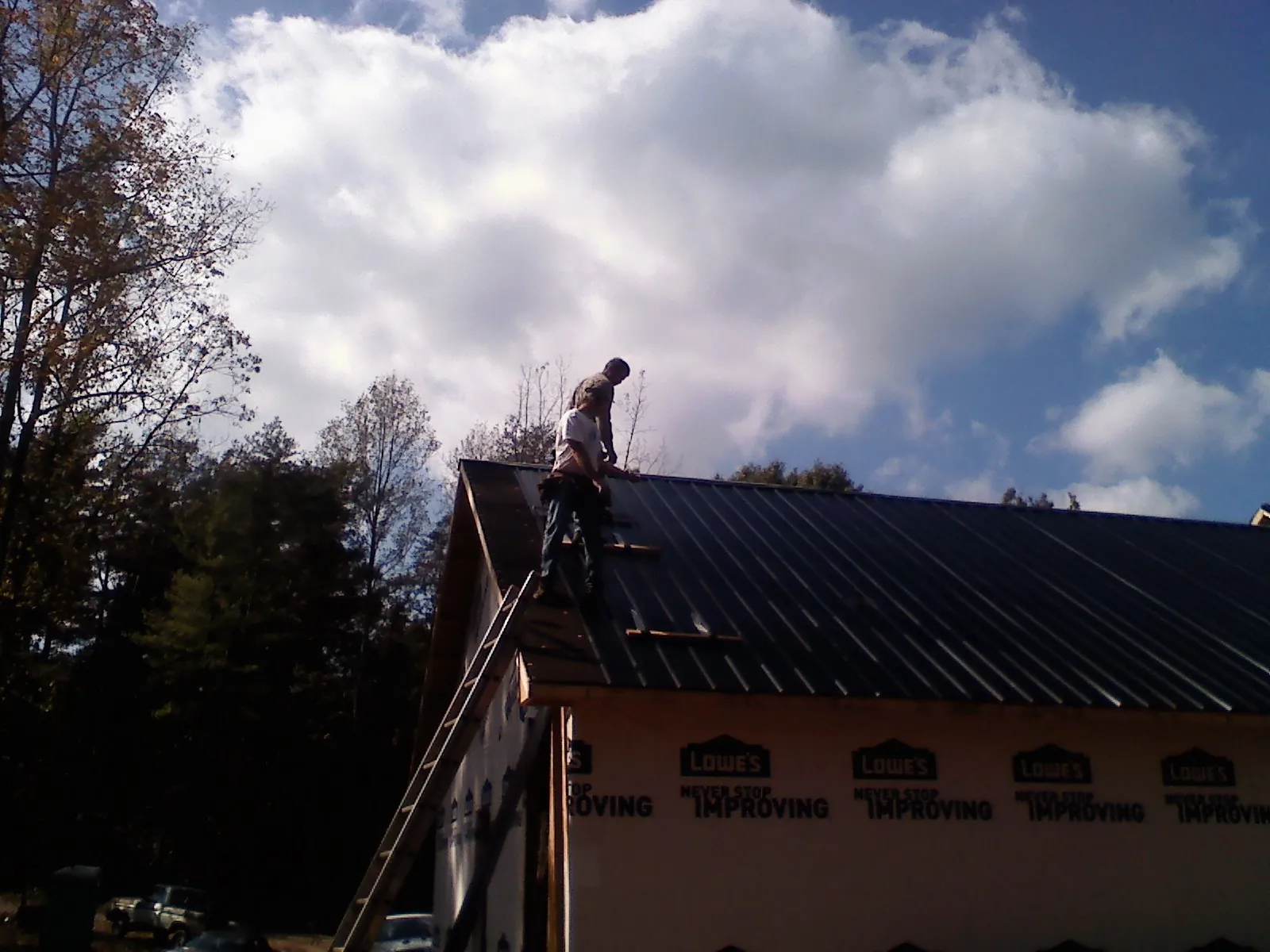 Roofer fastening dark metal panels high against a cloudy sky, from a Roof Inspection job in Nelsonville