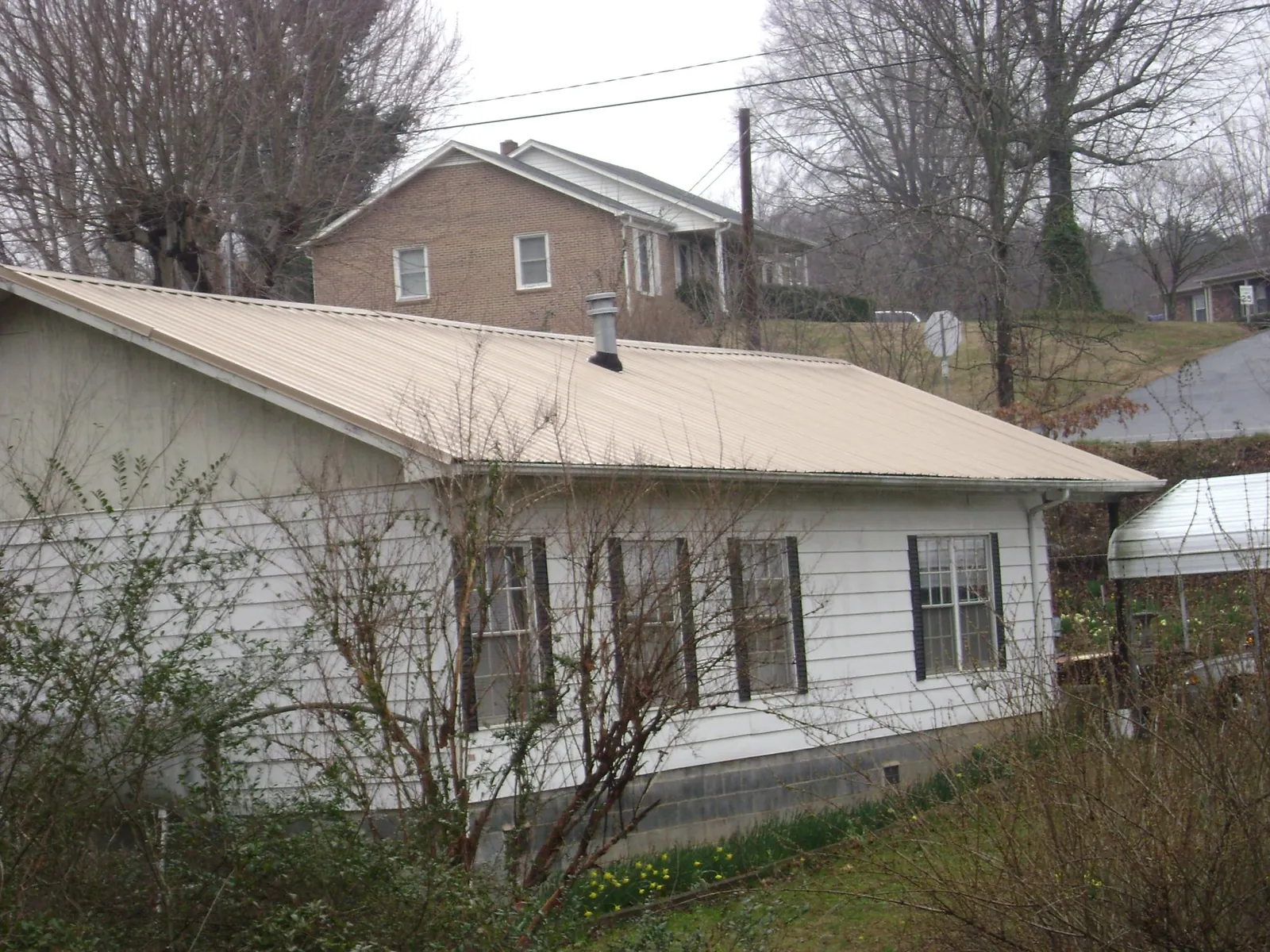 Tan metal roof on a white sided house set into a hillside — Commercial Roofing by Roofing Brothers in Nelsonville