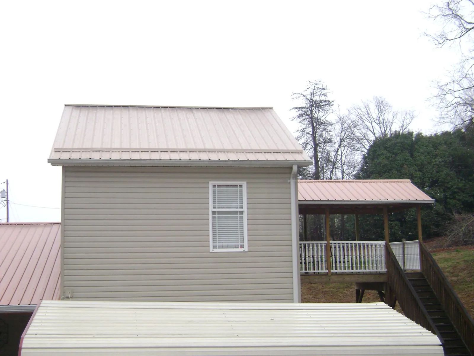 Tan metal roofs on a two story addition and attached porch, from a Roof Replacement job in Nelsonville